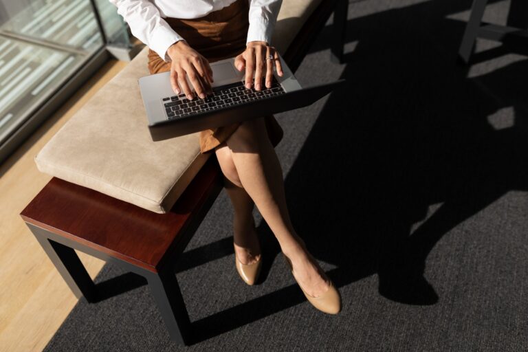 Low section of young Caucasian businesswoman using digital tablet while sitting on bench in modern office